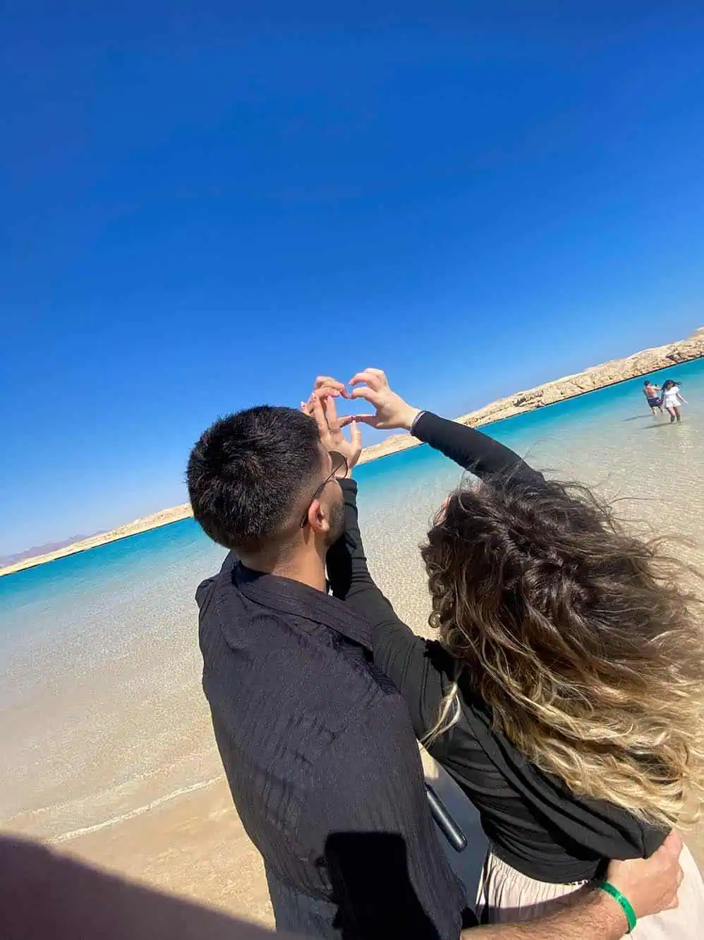 coppia di giovani di spalle fa il simbolo del cuore al lago magico sharm