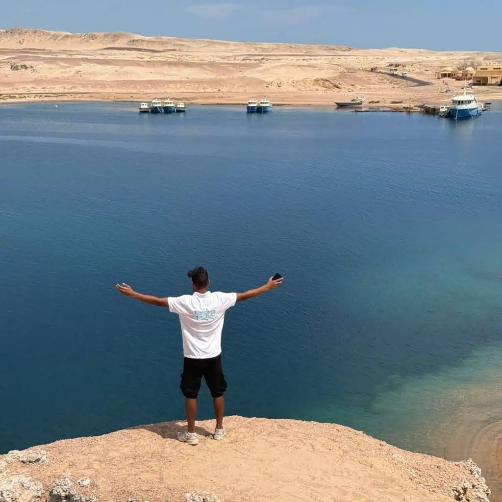 guida di buongiorno egitto con braccia aperte e mare sullo sfondo nel punto panoramico della baia dei barracuda in gita nel parco nazionale di ras mohammed