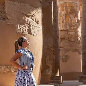 Woman in Luxor Temple admiring ancient carved columns in sunlight.